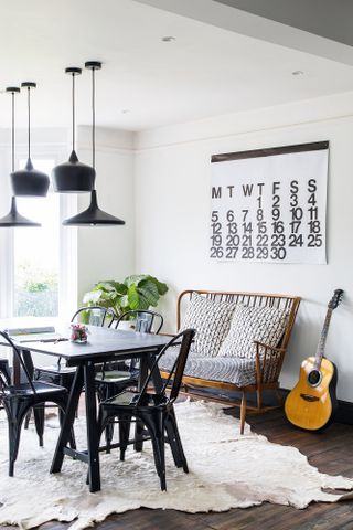 Light dining room in monochrome style with black dining table and chairs with a wooden sofa and guitar