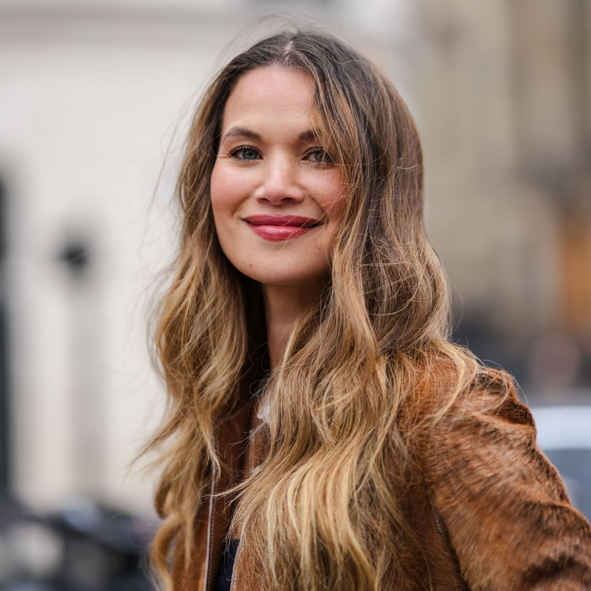 the best primers - street style shot of woman with long wavy hair and pink lipstick smiling