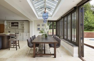 A large orangery kitchen extension with a dark wood dining table below blue pendant lamps