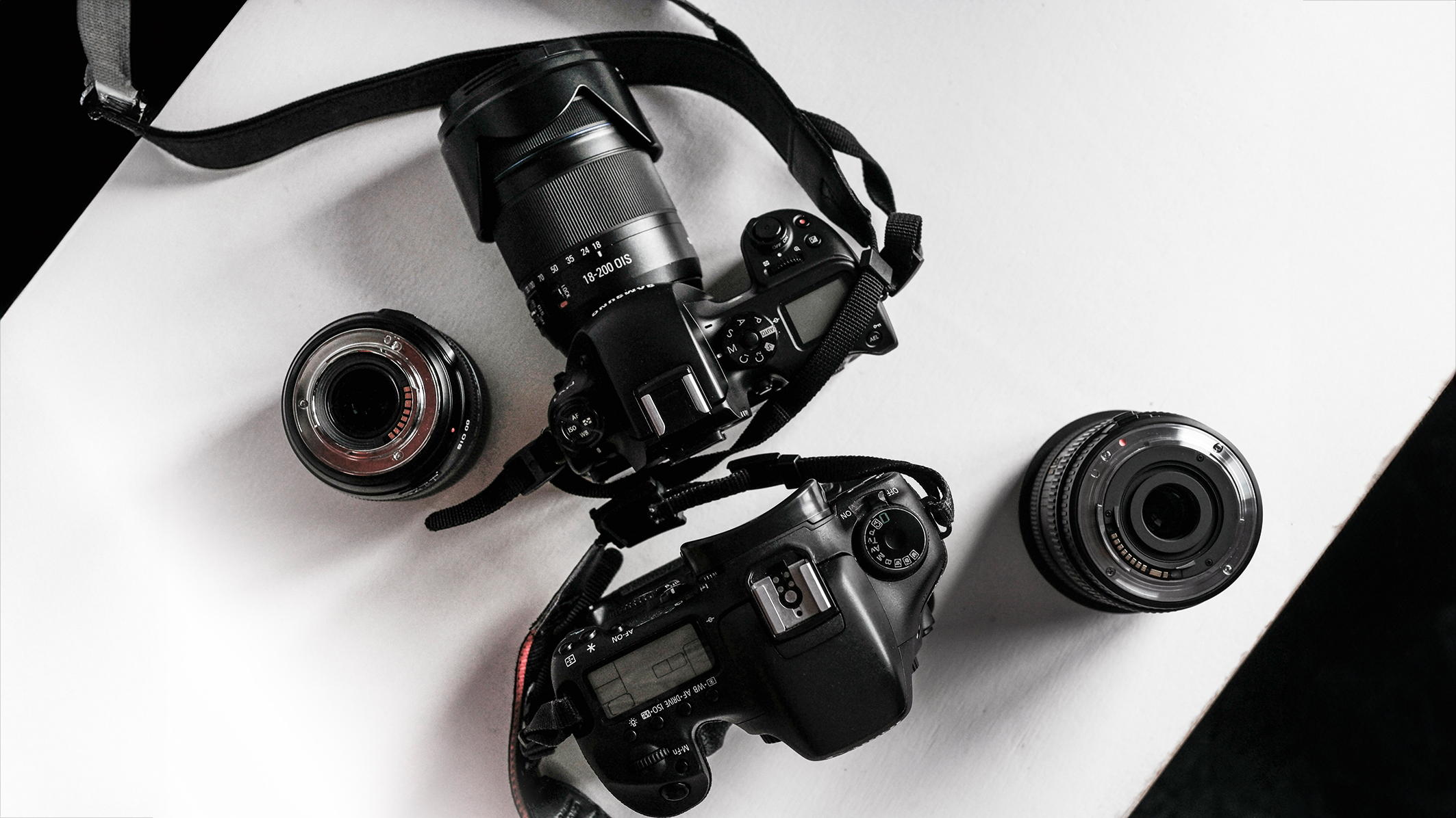 A top-down view of two DSLR cameras with different lenses on a white surface, showcasing their detailed designs and features