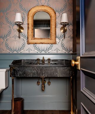 A statement bathroom with a marble sink, gold faucets, matching lights, mirror, teal and copper wallpaper and teal painted panelling