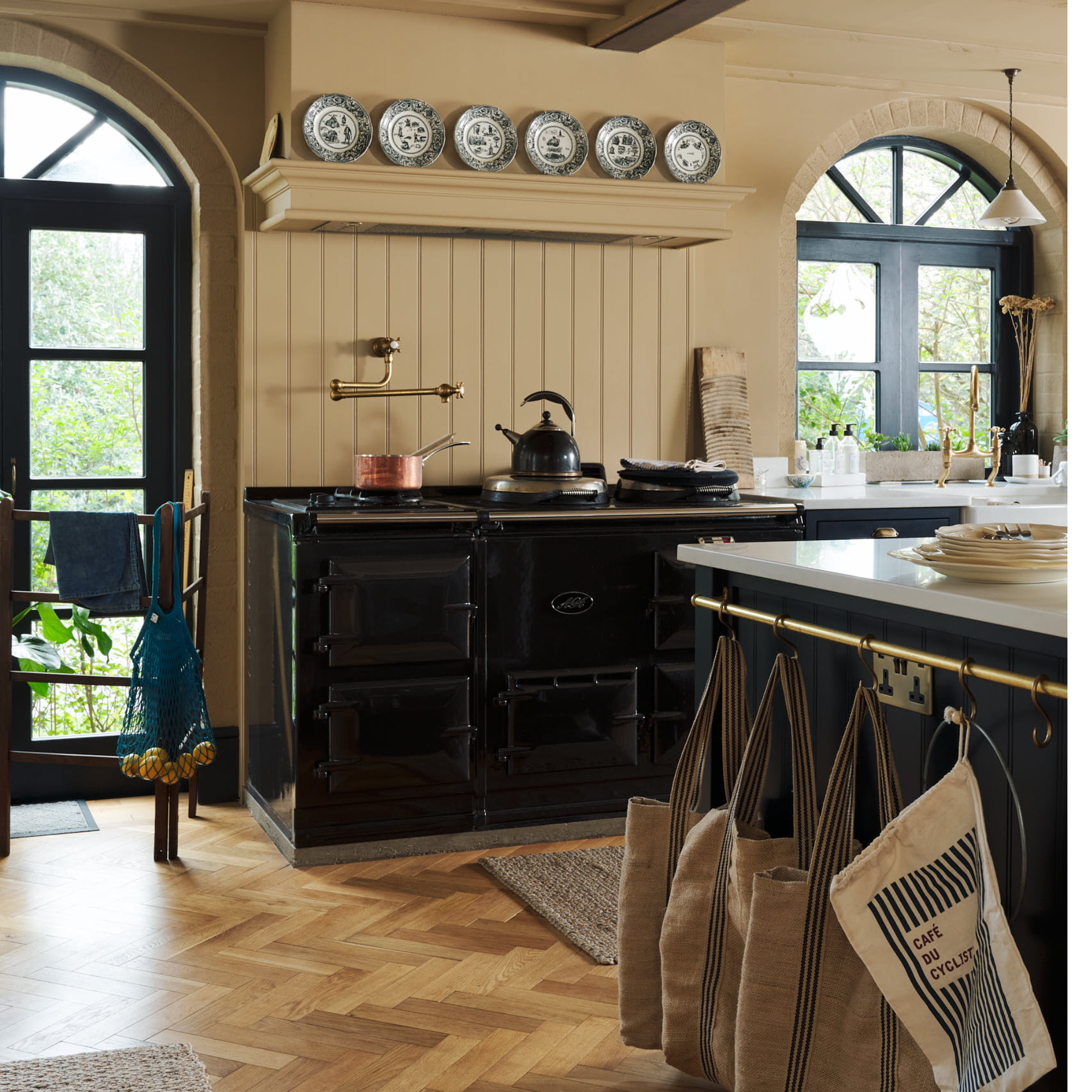 ochre kitchen with black island and Aga, white worktops, parquet flooring, hanging rail on side of island, tongue and groove walls