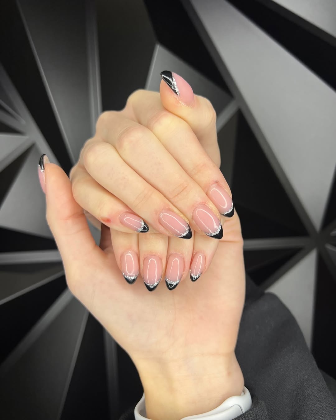 a person wearing a black french manicure with a glitter outline