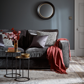 a grey sofa in a living room with red throw on arm