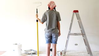 Person standing looking at painted wall with a roller in hand next to step ladder