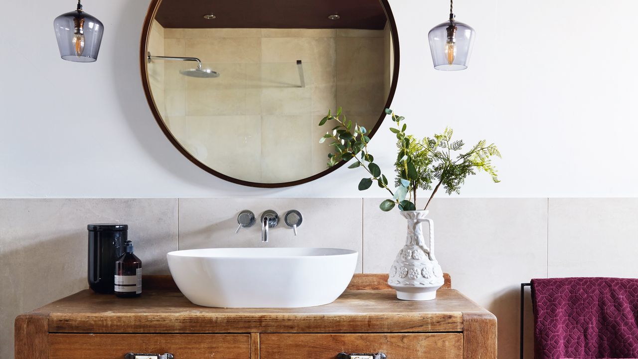 Bathroom makeover: close up shot of vanity unit in bathroom. Deep wood vanity unit with oval sink plumbed in and round mirror above