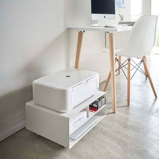 A home office setup with light grey laminate flooring, white desk, white and wooden office chair and tower printer stand with printer