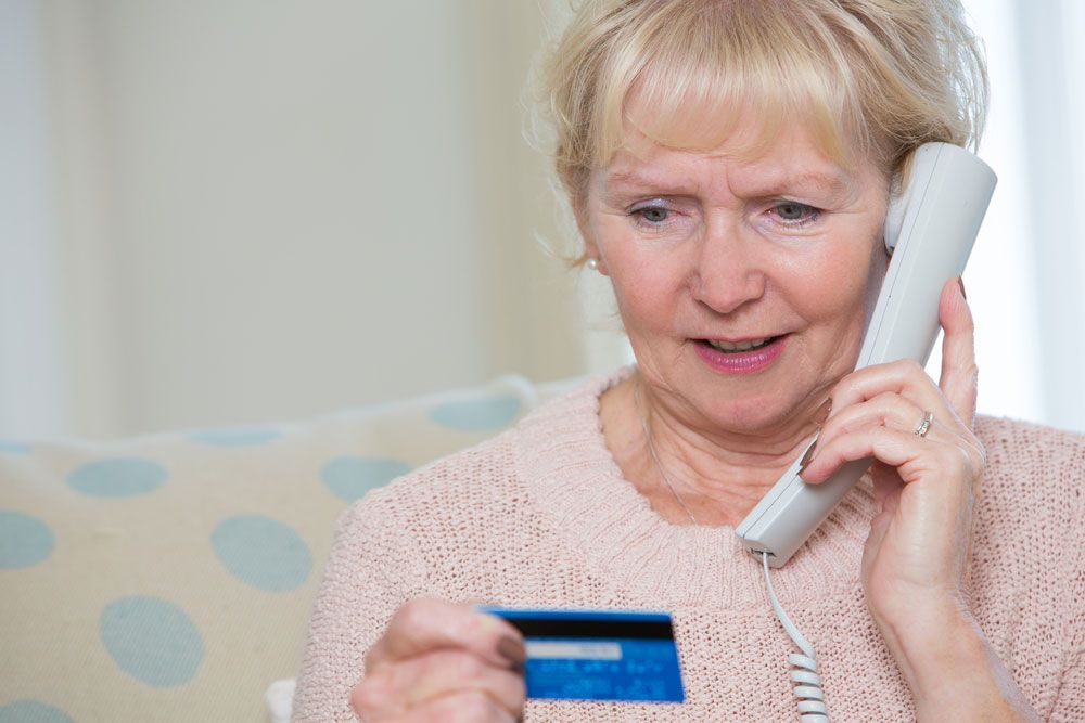 Concerned elderly woman reads payment card while holding phone.