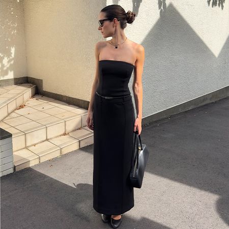 Illirida poses in black tube dress with long column like skirt, heels, and a handbag