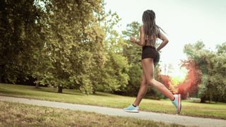 a woman running through a park in running shorts and a sports bra