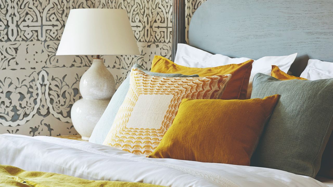 A bed with colourful cushions and bedside table lamp