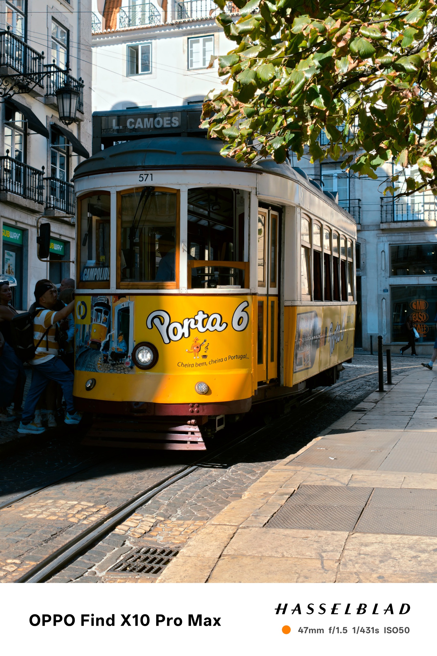 Yellow Lisbon tram traveling along tracks through a sunlit city street.