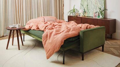 green Swyft sofa bed with orange duvet cover, timber side table, timber console table behind, with beige rug