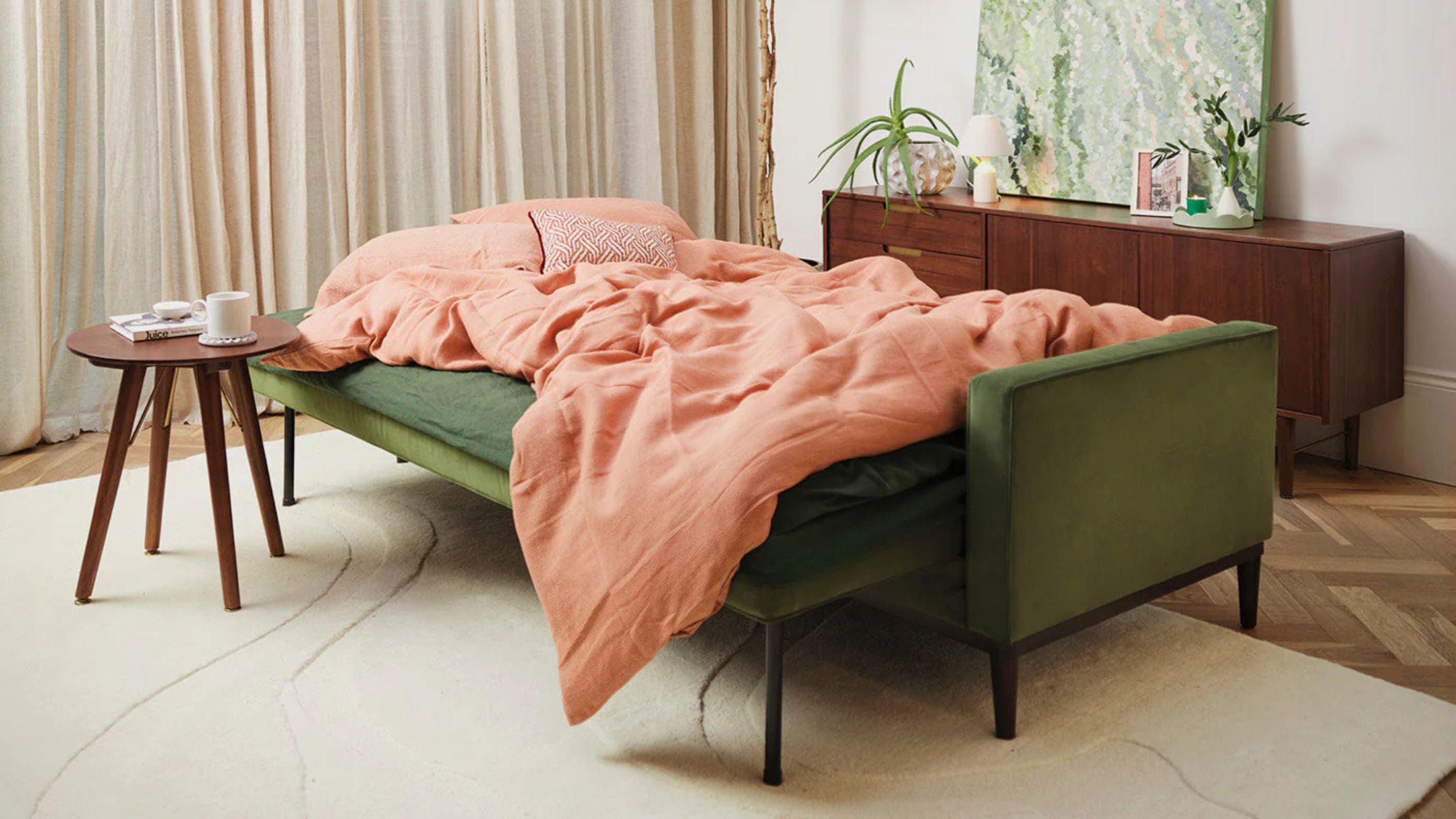 green Swyft sofa bed with orange duvet cover, timber side table, timber console table behind, with beige rug