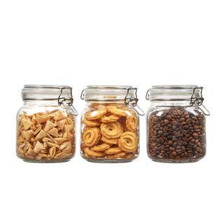 Three small glass storage cars filled with cereal, cookies, and brown coffee beans