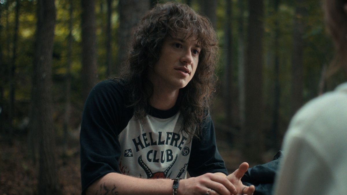 Joseph Quinn as Eddie sitting at a picnic table in Season 4 of Stranger Things.