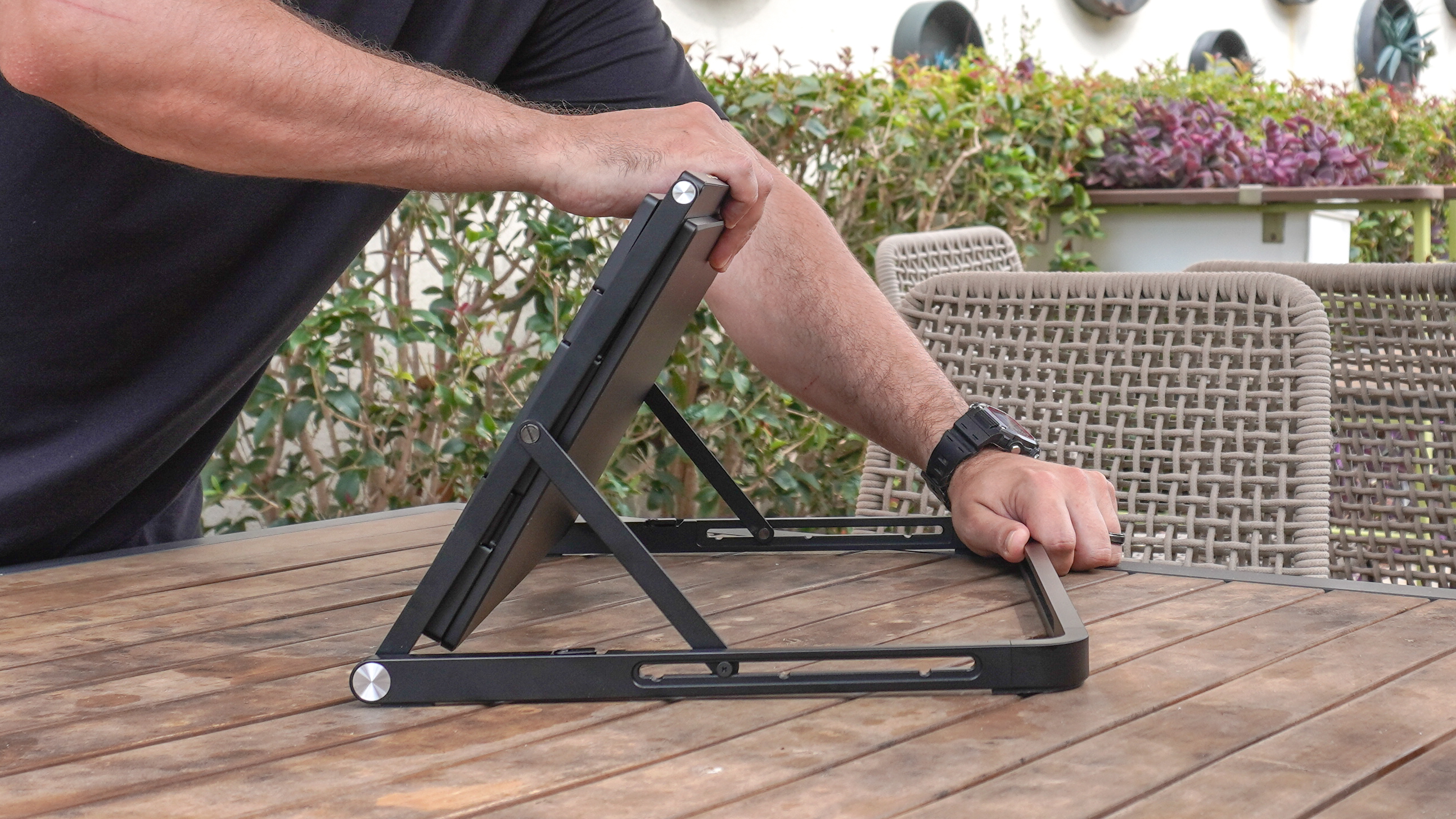 A person unfolding the Aura Triple Aero 15.6 Pro Max portable monitor on a table outside at a coffee shop