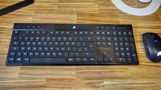 A black Corsair K100 Air Wireless keyboard on a wooden table