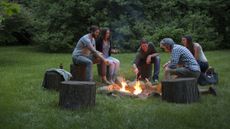 how to build a fire pit: Group of adults sitting around a fire pit in a field