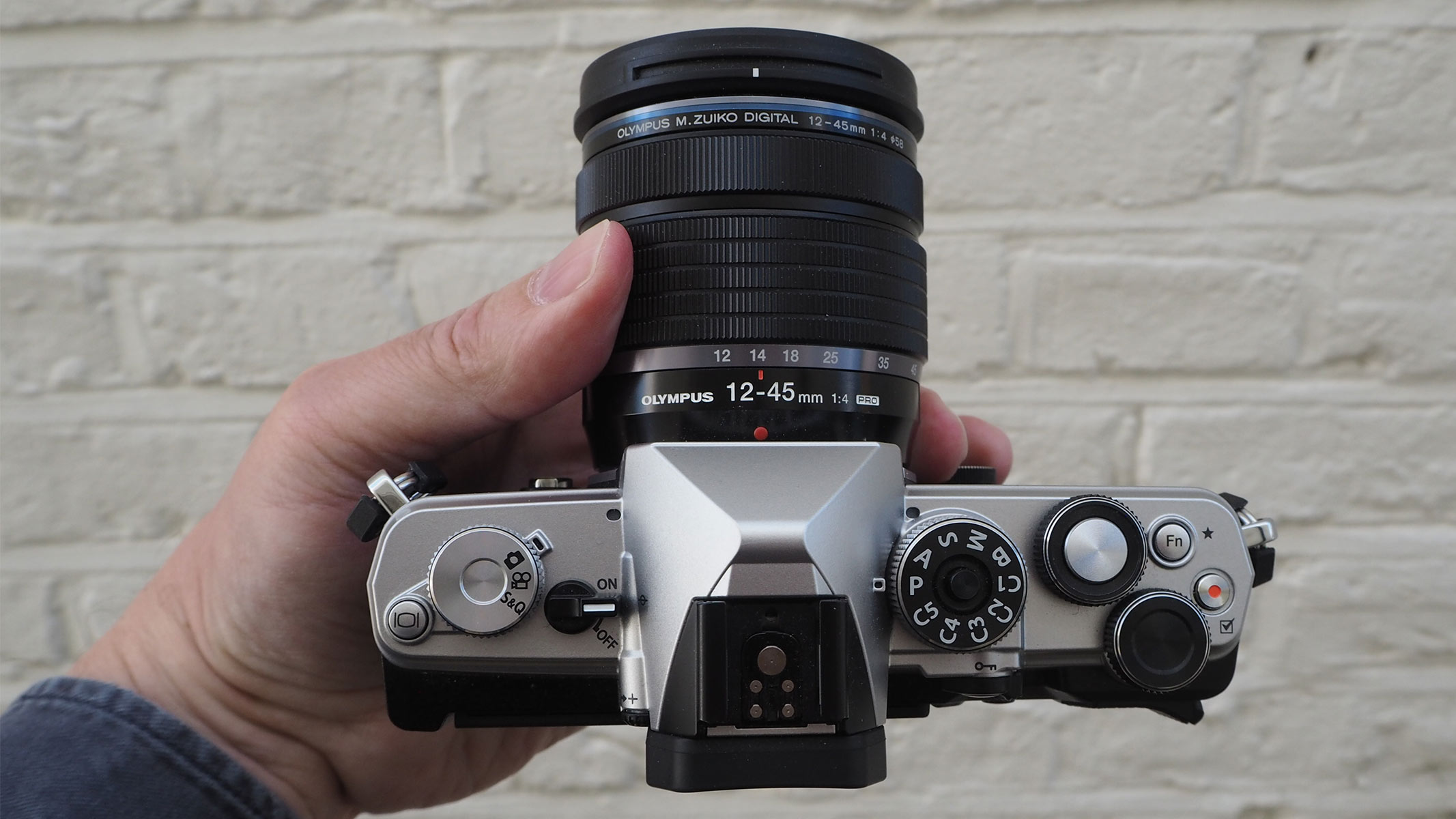 Reviewer holding the OM System OM-3 to show the top dials and switches.