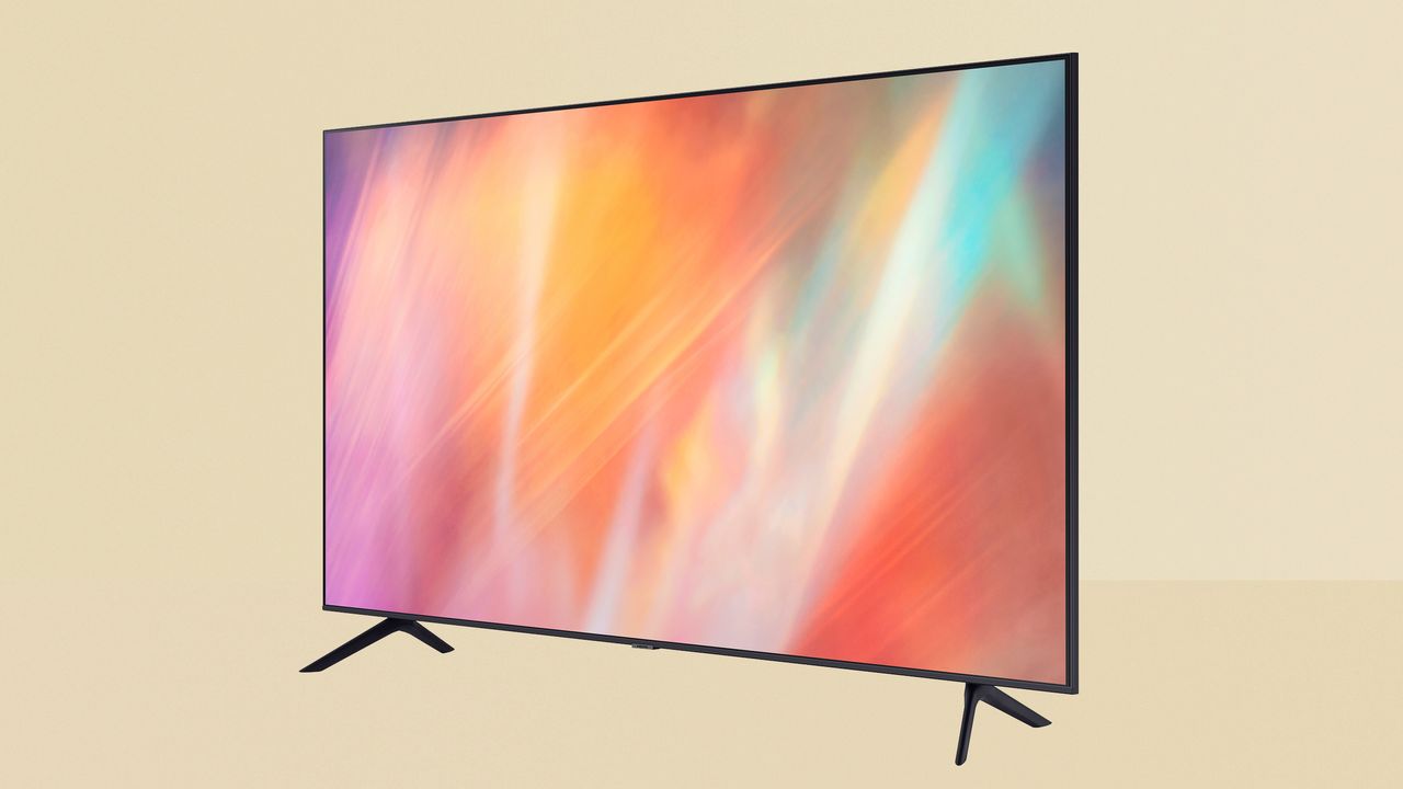 Samsung AU7100 review image showing the TV on a yellow background. The TV has a black frame with two arrow-shaped legs