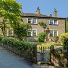 The exterior of a Grade II stone built house dating from the 18th century with a black gate leading to a front garden