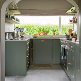Small kitchen with green base. units and large window with roman blind