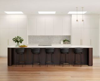 A kitchen with white cabinets and a dark island with 5 bar stools