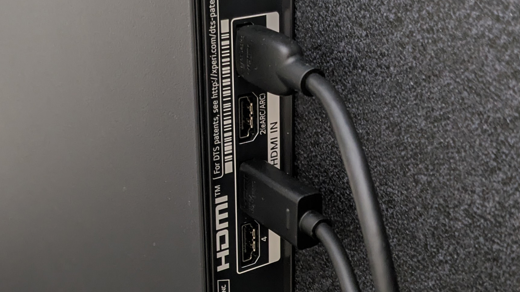A row of HDMI ports on the back of a TV, with two cables attached in specific ports, with an empty port labelled 'HDMI ARC'