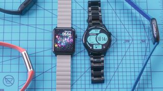 Two Armitron smartwatch models on a blue cutting mat with several Fitbit models off to the side of the image