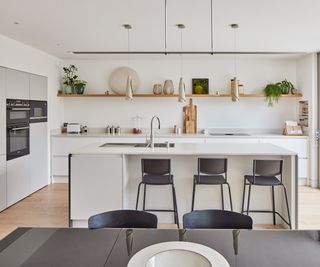 A contemporary kitchen with light walls, cabinets and surfaces. There are bar stools at the kitchen island