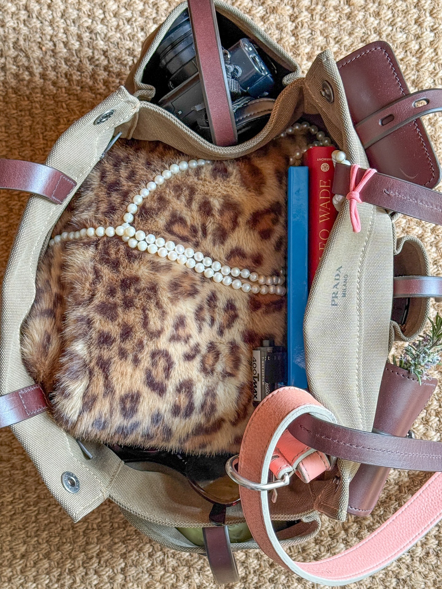 A green canvas Prada Route bag with a faux fur leopard print accessory inside and a pearl necklace.