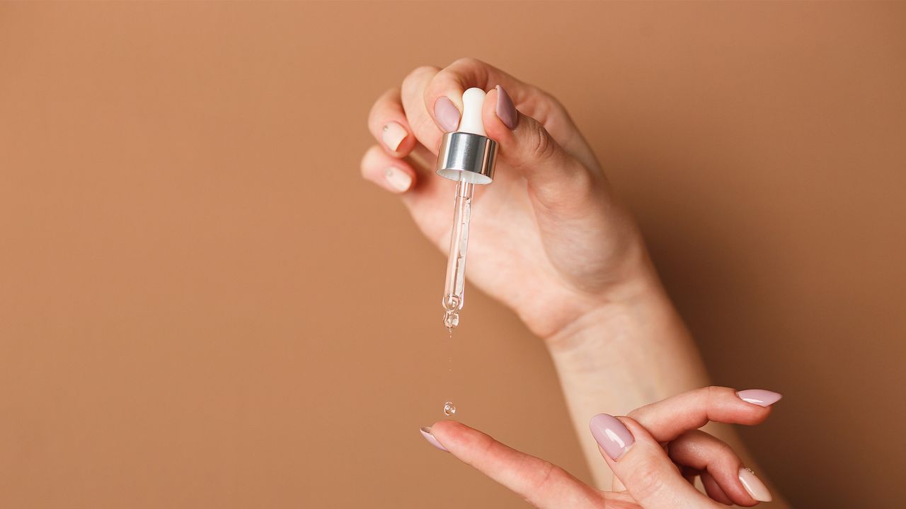 L&#039;Oreal pure retinol serum: Hands of cropped woman holding cosmetic serum pipette on the orange background.