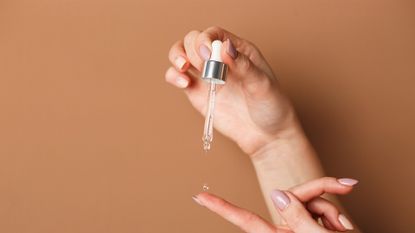 L&#039;Oreal pure retinol serum: Hands of cropped woman holding cosmetic serum pipette on the orange background.