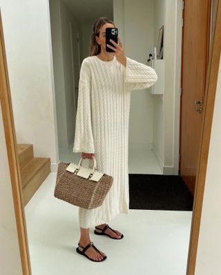 Woman takes photo in mirror wearing cream knit dress, basket bag and sandals