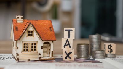 Miniature wooden house sitting next to a stack of coins and wooden blocks that say "Tax"