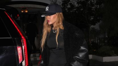 Rihanna wearing a little black dress with a black NY baseball hat and a black handbag