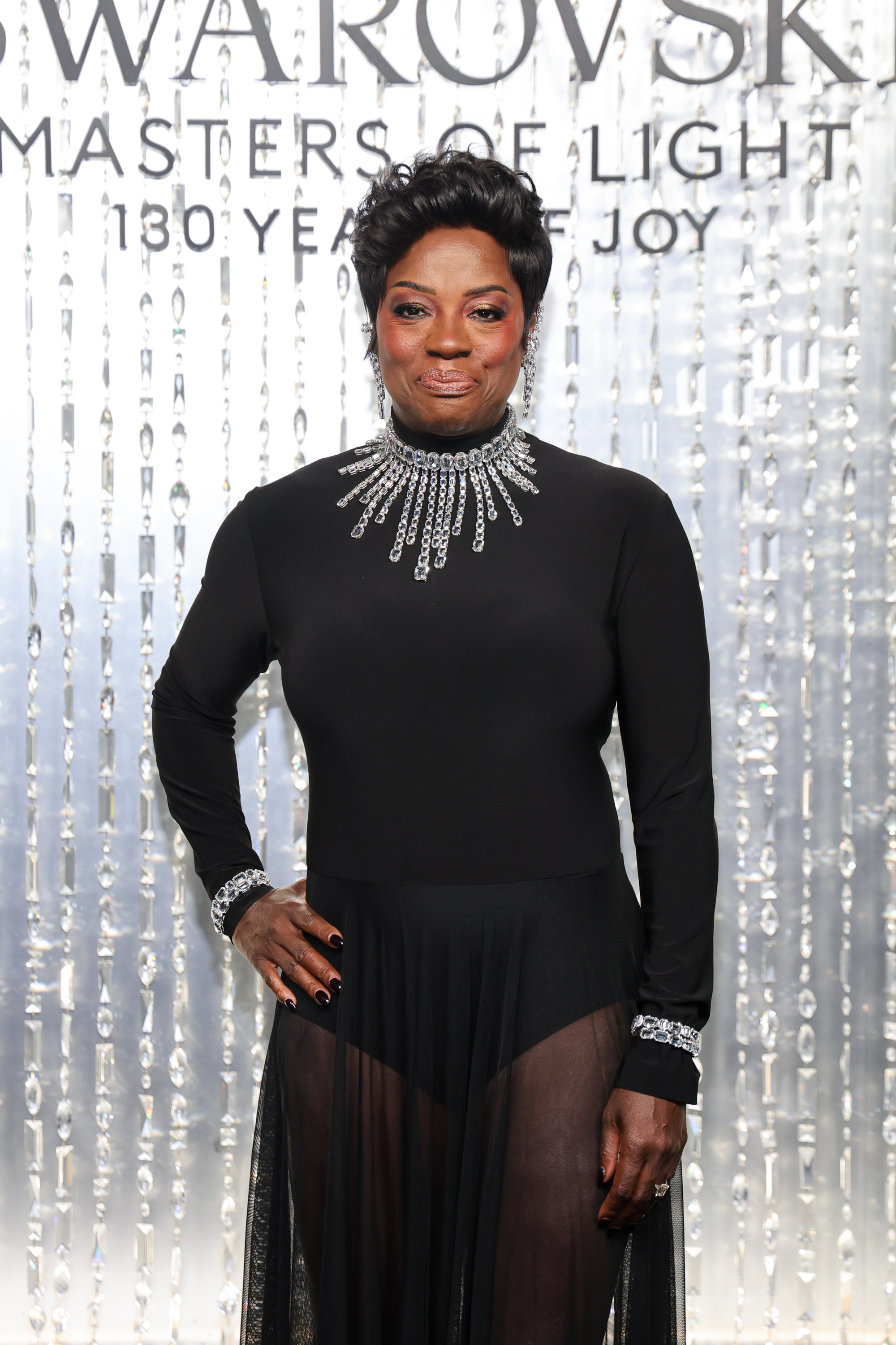 Viola Davis wearing a pixie hairstyle, a black dress with a sheer skirt detail, and a black manicure.