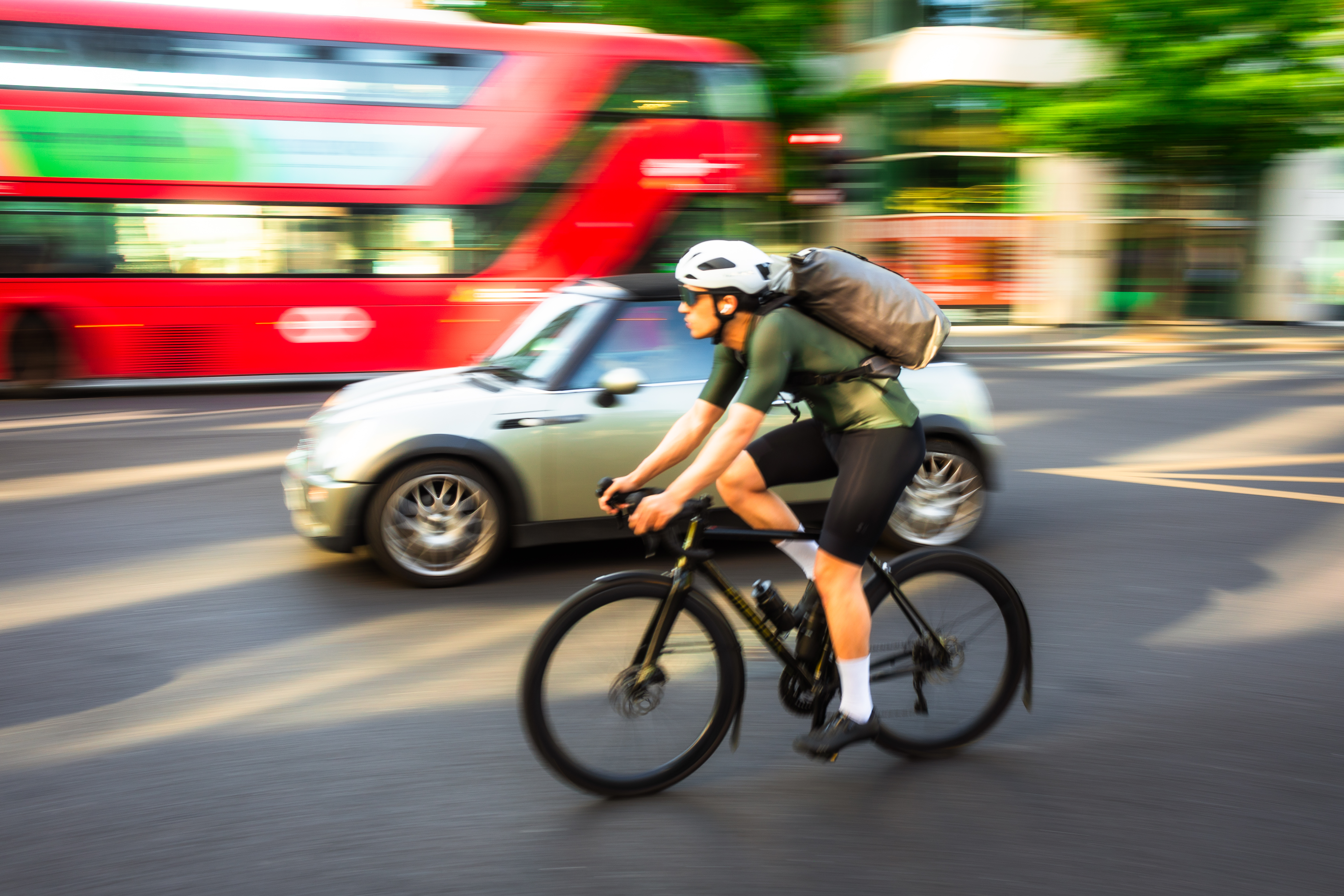A man in lycra on a black bike cycles past a green car in London
