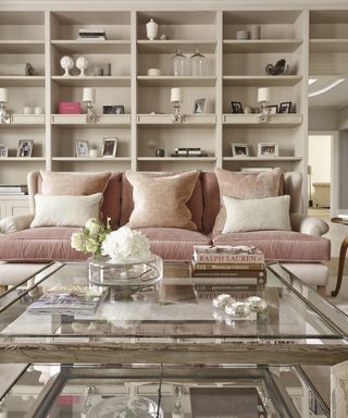A pink sofa in front of large white wall shelving and a coffee table