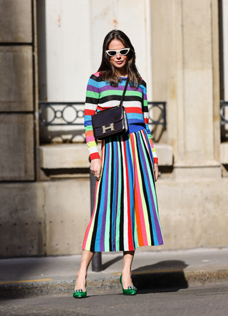 Therese Hellström @tesshell wears white cat-eye sunglasses, a multi colored striped wool midi dress with long sleeves, a brown leather Hermes bag, green pointed shoes with metallic pearls, on April 08, 2021 in Paris, France