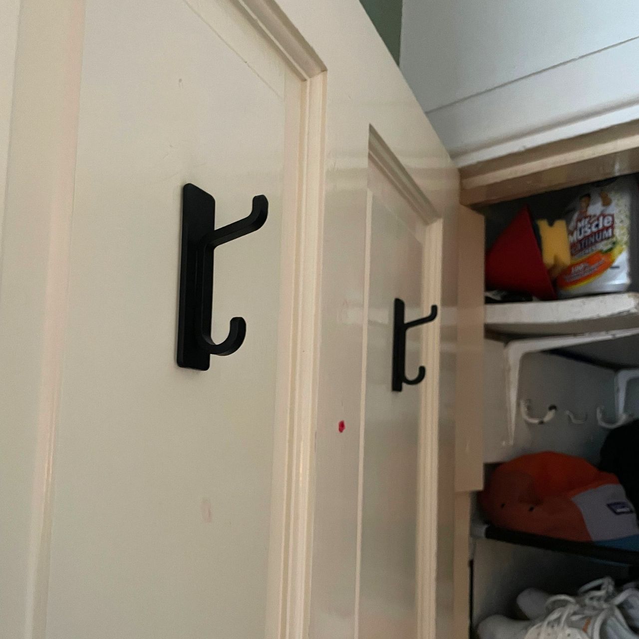 Black hooks stuck onto the door of an under-the-stairs cupboard
