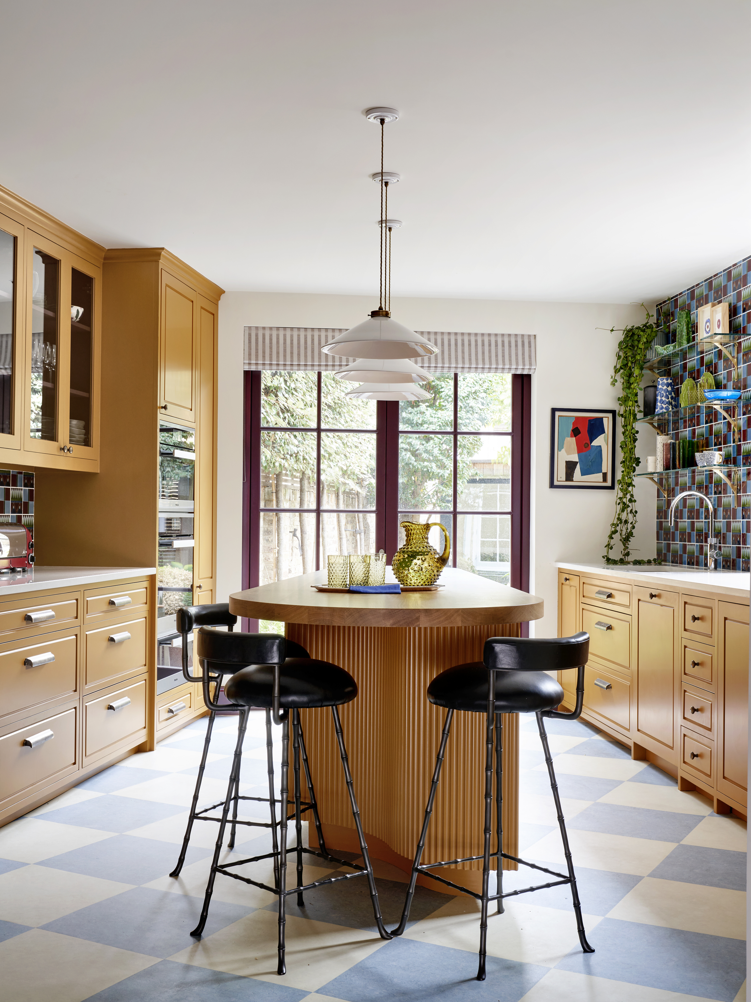 A kitchen with yellow painted cabinets, yellow island, black island chairs, and three lights suspended above