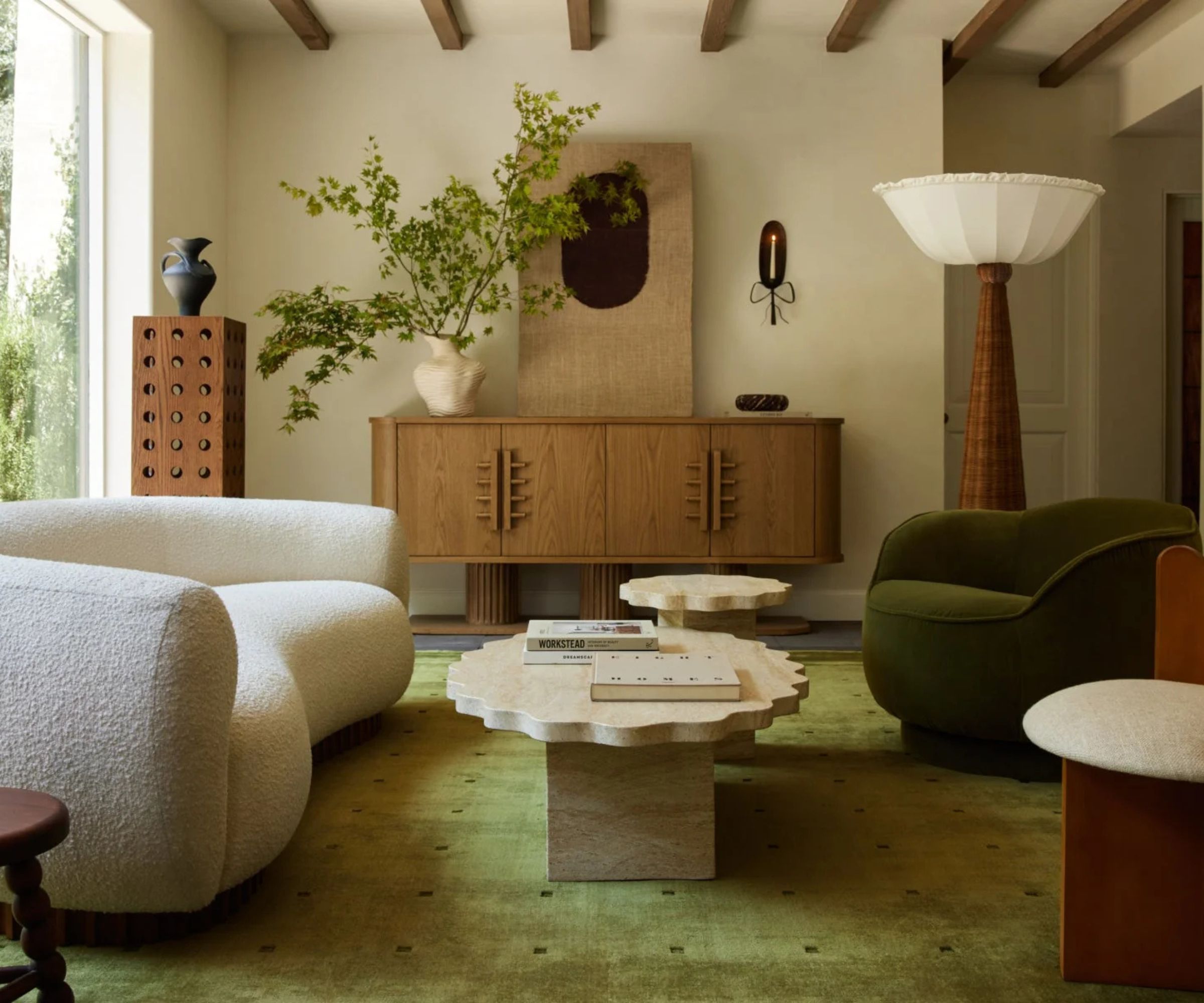 Cream living room with wooden beams. A cream boucle curved sofa is on the left and a green curved armchair on the right with a stone ways coffee table in the middle. A green rugs sits in the middle