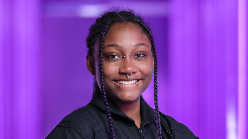 A young black woman smiles for a portrait photo against a purple background.
