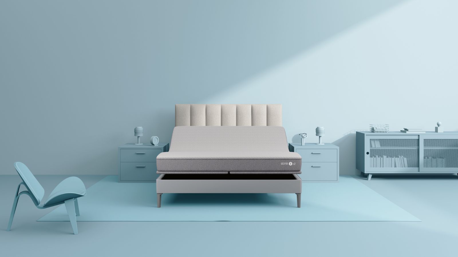 Sleep Number c2 mattress on a light grey bed with fluted headboard, against a pale blue wall. The nightstands, chair, cabinet, and accessories are all the same shade of blue.