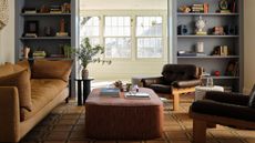 a small living room in new jersey with large windows, custom blue bookcases, a west elm rug, and vintage style 1970s sofa and leather armchairs
