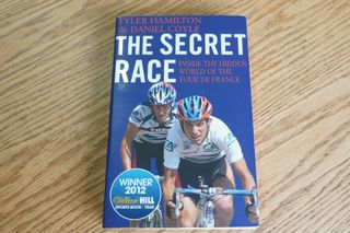 The best cycling books includes The Secret Race and shows an image of forward facing racing cyclist Tyler Hamilton at the front and Lance Armstrong behindon a blue background