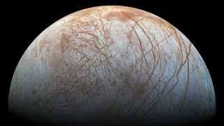 jupiter's moon europa, its icy surface criscrossed by dark reddish-brown lines, against the blackness of space