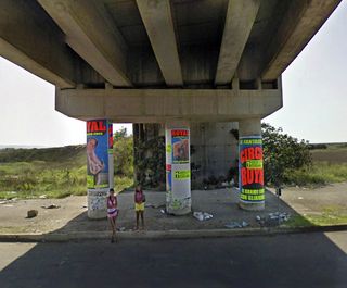 Two women standing under concrete bridge in front of pillars with posters on